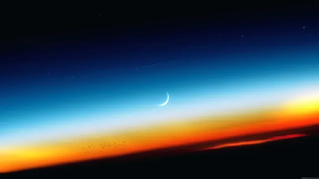 A crescent moon above a landscape at sunset