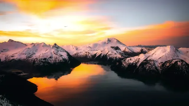 Golden sunset on snowy mountain peaks reflected across a calm fjord