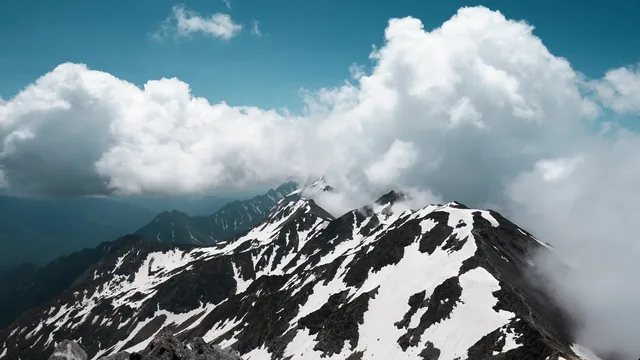 Rugged snowy mountain peaks beneath a broad sky filled with slow clouds.