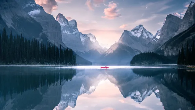 Lone fisherman on a clear reflective lake surrounded by tall mountains.